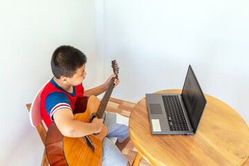 The story of a boy watching a notebook computer while preparing to practice playing guitar at home....