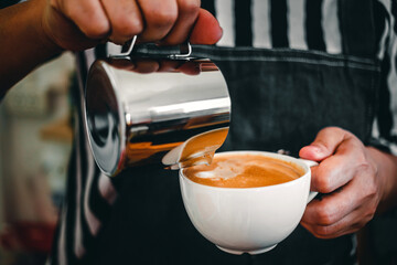 Close-up of the hand of a professional barista in a coffee shop making  pouring steamed milk into the coffee cup making latte menu