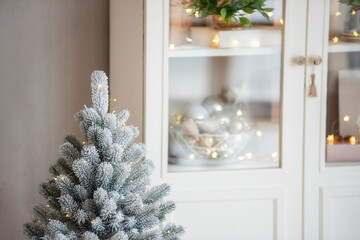 Snow-covered, undecorated artificial Christmas tree stands in front of a blurry wooden sideboard