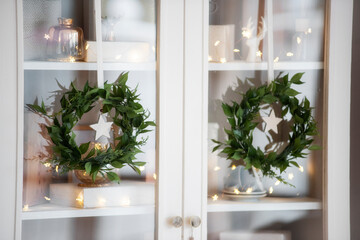 Scandinavian interior style, green wreaths hang on a white sideboard. Christmas tree in a pot.