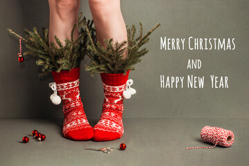 Merry Christmas and Happy new year creative greeting card. Female legs in red woolen socks with ornaments and minimal decorated fir branches on green background. Creative Christmas tree concept