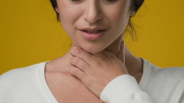 Close up sick female studio yellow background Indian ill woman girl lady suffer pain ache throat painful swallowing tonsillitis thyroid gland touching neck bacterial diseases COVID-19 coronavirus