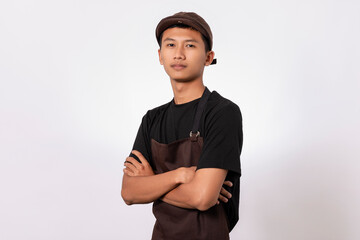 Handsome barista asian man wearing brown apron and black t-shirt isolated over white background standing with crossed arms smiling confident looking at camera