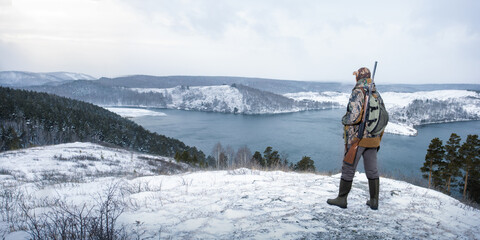 Hunter in camouflage with shotgun on the winter hunting. panoramic view with copy space.