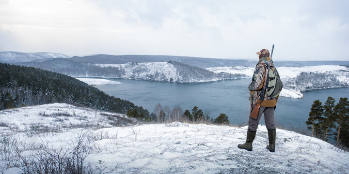 Hunter in camouflage with shotgun on the winter hunting. panoramic view with copy space.
