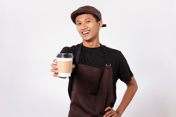 Handsome barista asian man wearing brown apron and black t-shirt isolated over white background. Barista holding coffee cup, serving coffee to customer - obrazy, fototapety, plakaty