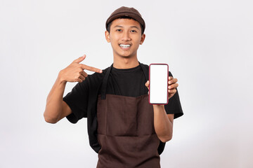 Handsome barista asian man wearing brown apron and black t-shirt isolated over white background holding smartphone with white blank screen for mockup. Sales offer and application Recommendation