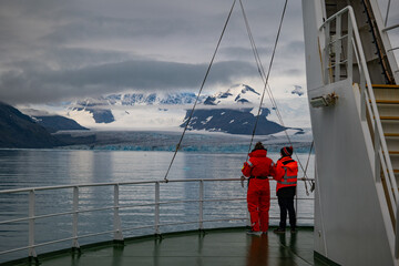 Two persons on the bow of a ship looking over the water at glacier and mountains