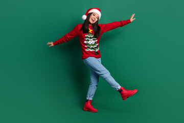 Full length photo of funny carefree lady wear red ugly print xmas sweater cap walking isolated green color background