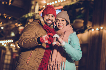 Photo of excited sweet girlfriend boyfriend showing arms heart walking outdoors urban city market