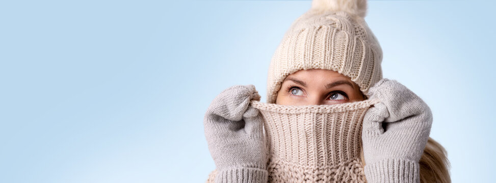 woman in knitted wool clothes hiding her face in sweater and looking up isolated on blue background. winter fashion. warm clothing. banner with copy space