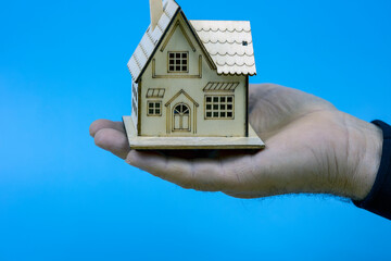 Toy wooden house in hand on a blue background. copy space