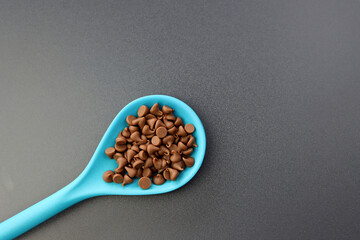 Chocolate droplets in a blue spoon on a gray background. Sprinkles for decorating confectionery.