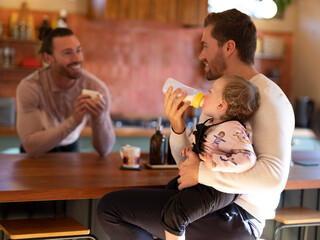 Gay couple feeding baby daughter in kitchen