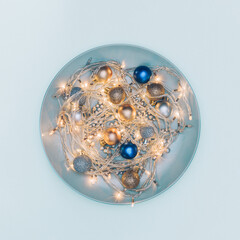 Minimal Christmas concept with round plate filled with Christmas lights and shiny baubles on blue background