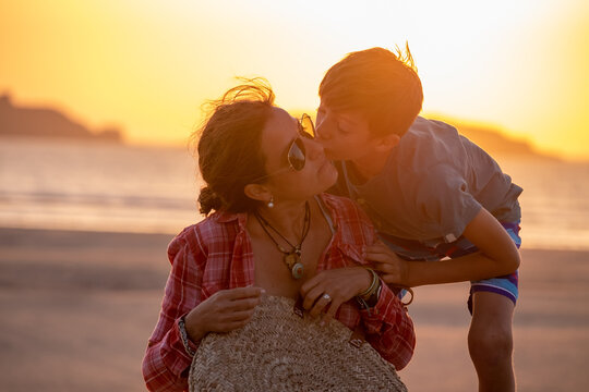 A boy kissing his mother in a sunset by the sea