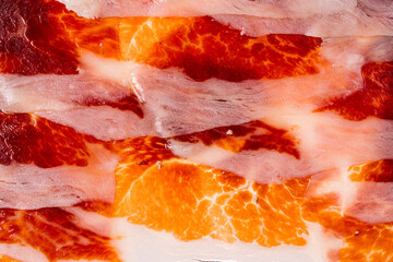 Close-up of juicy meat slices of spanish jamon, abstract pattern of slices of jamon iberico (serrano ham) for background and screensaver, macro texture of thin slices of meat, flat lay
