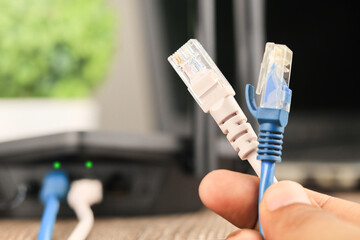 Hand holding Blue and white  Cable Network  RJ45 Lan Internet. router and laptop placed on a wooden...