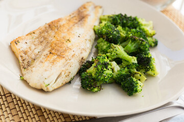 fried fillet of sea bass with garnish of broccoli on black warm stone plate