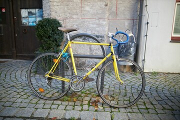 Side view of yellow bicycle locked onto a metal structure on cobblestone sidewalk