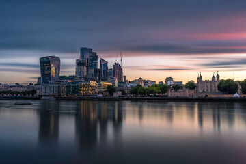 Fototapeta na wymiar The city and Tower of London, at sunrise. Long exposure to smooth out the river Thames. The building are reflecting in the water