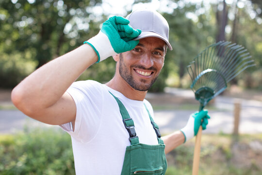 friendly male gardener with rake tipping his cap in greeting