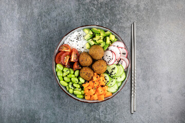 Buddha bowl with rice, falafel, green beans, cherry tomatoes, avocado, cucumbers, black sesame on a gray background. Vegan poke bowl with falafel and vegetables. Top view. 