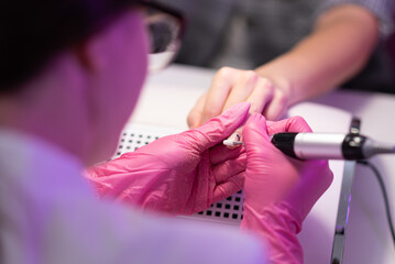 Fototapeta premium Close-up of a girl doing a manicure in a beauty salon. Nail care. Manicurist in pink gloves removes gel polish from nails with a fresco. Hardware manicure close-up. cosmetic procedure