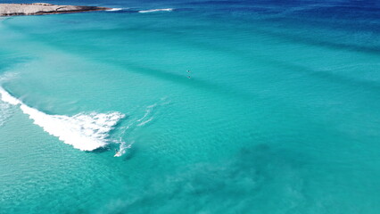 Drone footage of surfers waiting for waves in Esperance Australia. Amazing blue clear water. 2 surfers on surfboards in the ocean. Foamy wave in the front.