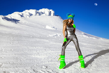 Sexy woman in silver cosmic outfit silver and winter boots is posing in the mountains. Female model in glamour silver jumpsuit in winter scenery.