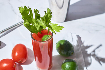 Bloody or virgin mary cocktail served in a cup with celery sticks on a white marble background