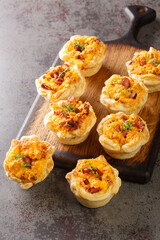 Freshly baked puff pastry cups stuffed with eggs, cheese and ham close-up on a wooden board on the table. Vertical