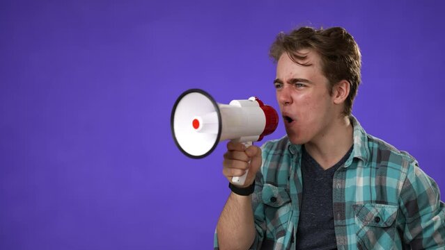 Side profile view of excited young man 20s years old in casual shirt isolated on purple background studio. People lifestyle concept. Screaming in megaphone looking aside camera