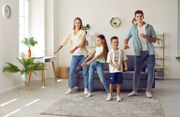 Happy family having fun together with little son and daughter in modern living room. Young dad and mother with adorable cute children dancing funny and enjoying weekend at home. Happy family concept.