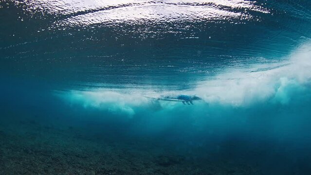Surfer does duck dive. Underwater view of the male surfer diving under the wave with surfboard