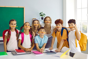 Portrait of happy school children and teacher with pencil mustaches. Group of junior students and...