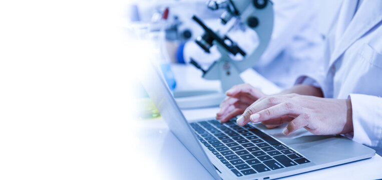 Close-up view of a scientist or student using a laptop computer and a microscope. science concept - Powered by Adobe