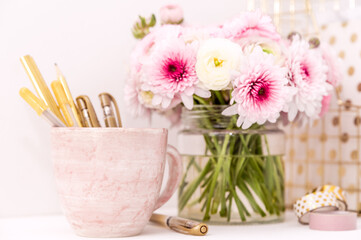 Fototapeta na wymiar A femininely styled desktop in shades in gold and dusty pink with modem stationery. Lifestyle theme inspired by the office workspace of a stylish woman. With fresh flowers including Ranuculus