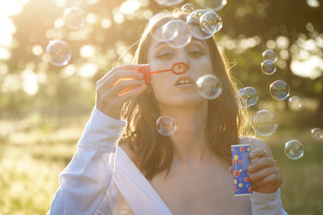 Beautiful woman blowing soap bubbles in a field on a beautiful summer day	
