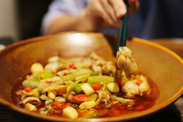 close up hand using chopsticks to pick bullfrog meat from a plate of spicy Sichuan cuisine