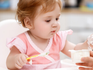 Beauty baby girl . A mother feeds her young daughter. Children's cottage cheese or porridge . Child watches with interest . Concept of dietetics for babies and healthy food . Motherhood and childcare