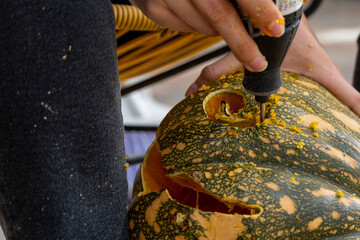 young man with a drill or dremel drilling a pumpkin for halloween