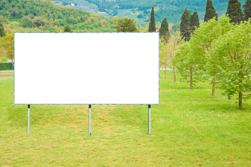 Blank billboard against a green mowed lawn with trees in the countryside - image with copy space