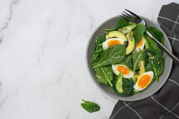 Fresh green salad with egg, avocado and spinach on a gray background in a gray plate.