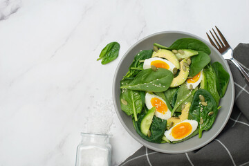 Fresh green salad with egg, avocado and spinach on a gray background in a gray plate.