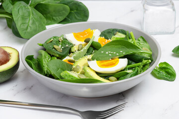 Fresh green salad with egg, avocado and spinach on a gray background in a gray plate.