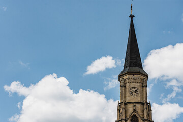 Fototapeta na wymiar Roman Catholic church tower with a clock in a gothic architectural style against clouds