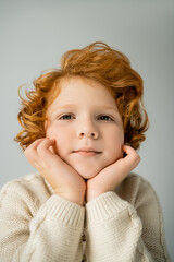 Redhead boy in warm beige jumper looking at camera isolated on grey © LIGHTFIELD STUDIOS