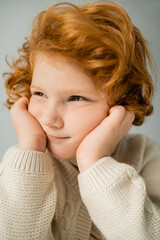 Portrait of red haired kid in beige knitted jumper looking away isolated on grey