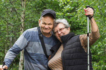 Happy senior couple tourists walking with trekking sticks in the mountain forest. Active seniors concept. Healthy life